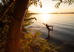 Eine Frau macht Yoga in einem See im Sonnernuntergang. Es ist blauer Himmel und warm