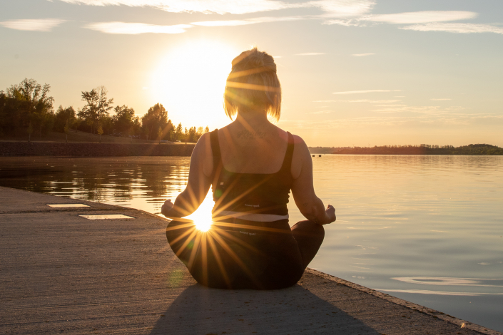 Eine Frau macht Yoga in einem See im Sonnernuntergang in NRW.
