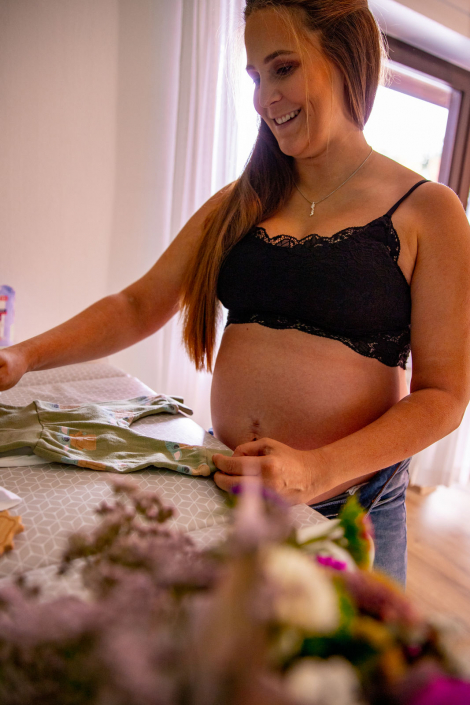 Eine werdende Mutter steht glücklich mit nacktem Babybauch an einem Wickeltisch.