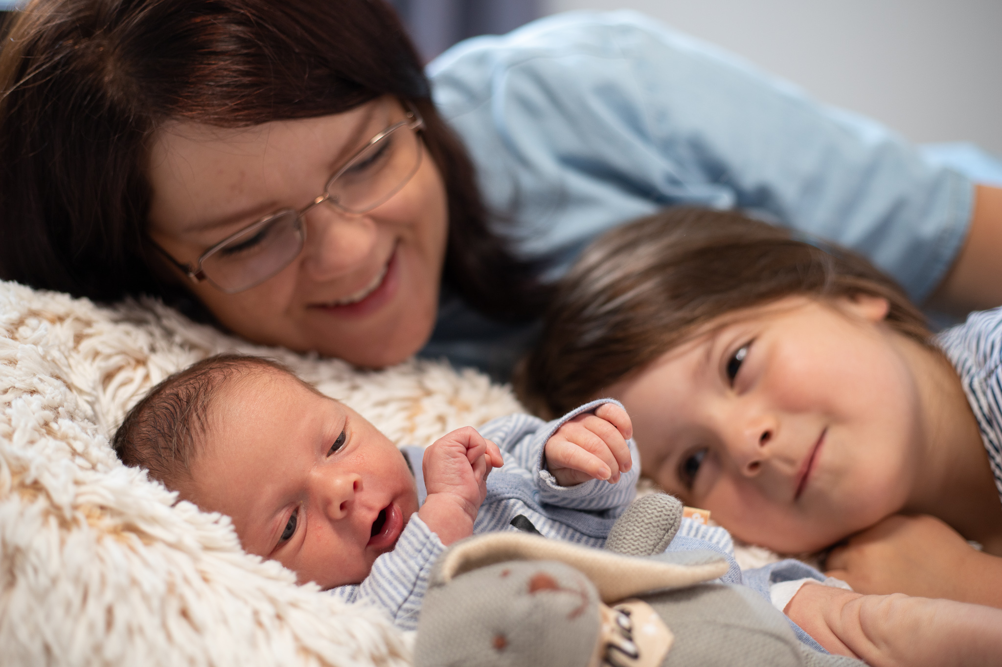Eine glückliche Mutter liegt mit Ihren beiden Kindern in einem Bett bei einem Fotoshooting in NRW