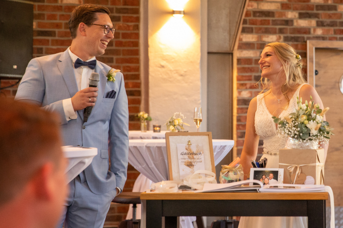 Ein Ehepaar hält eine Rede auf der eigenen Hochzeit. Sie schauen sich an und sind glücklich.