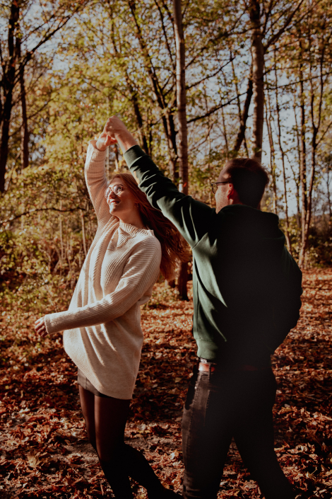 Ein glückliches Paar tanzt im Herbst bei einem Fotoshooting im Wald. Es ist goldene Stunde, die Sonne geht gleich unter.